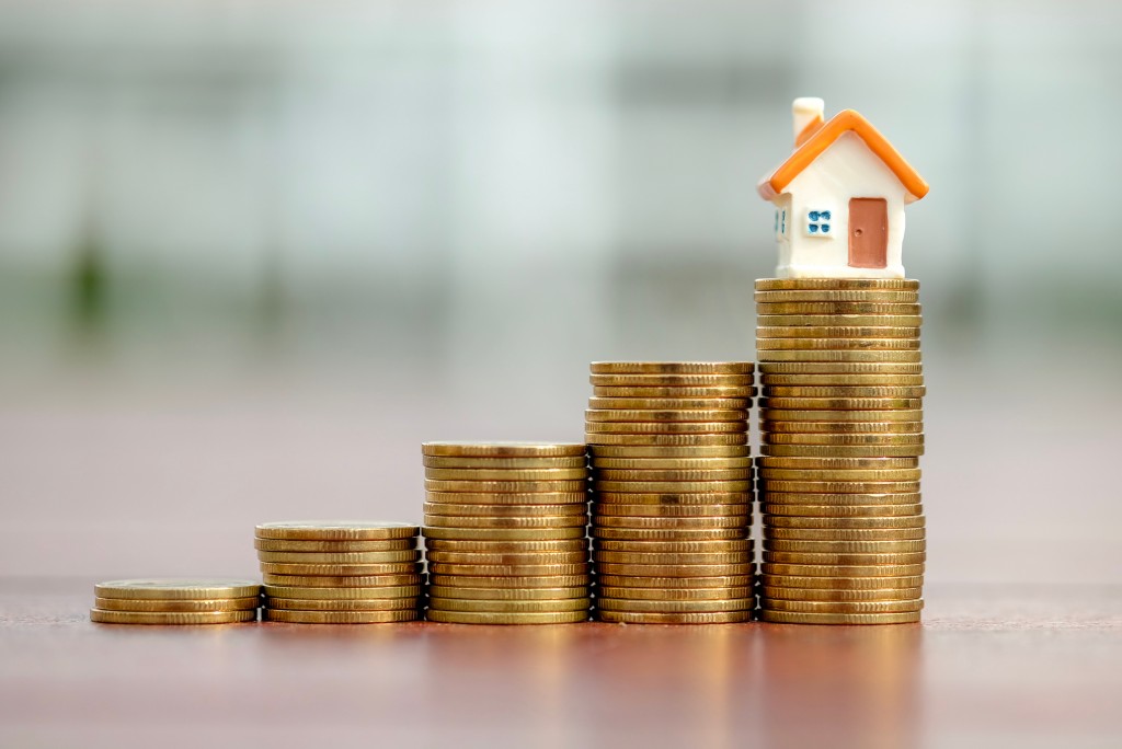 stack of coins getting taller with a miniature house on top of the talles stack