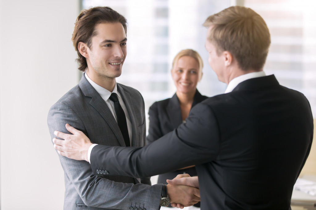 a businessman shaking hands and tapping the arms of a young employee