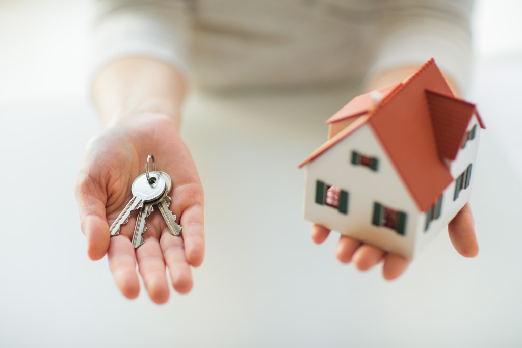 A woman holding a set of keys and a small house, symbolizing her selling of her property