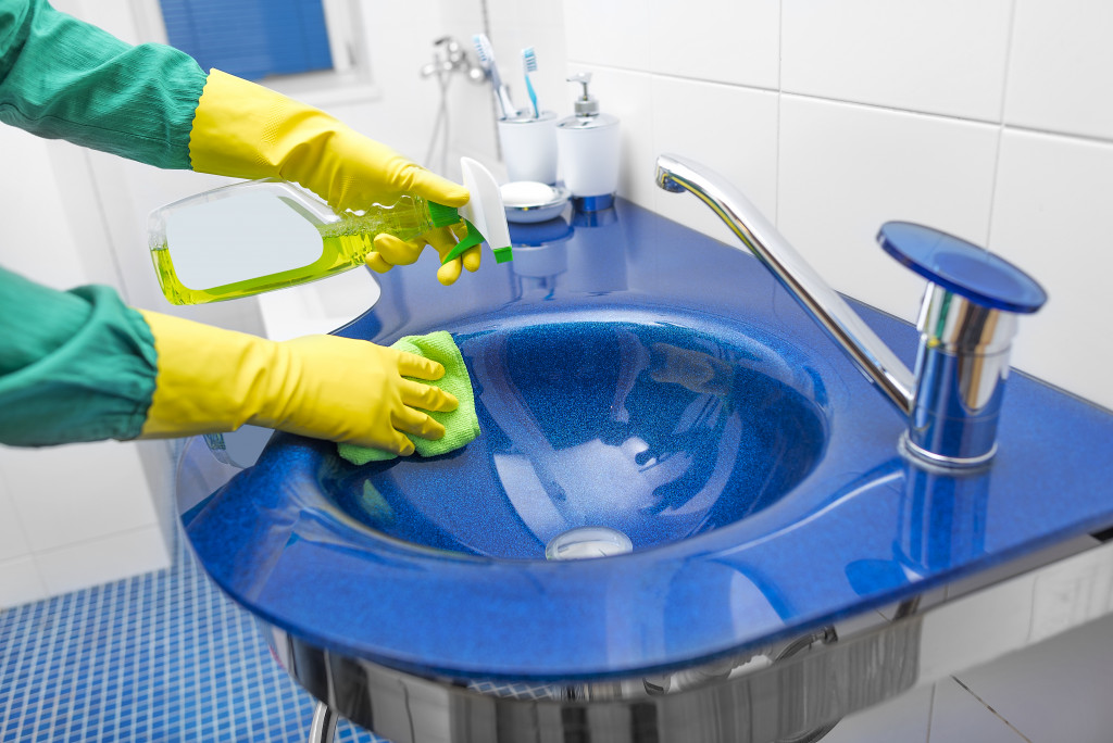 Hands in yellow gloves washing the sink with detergent