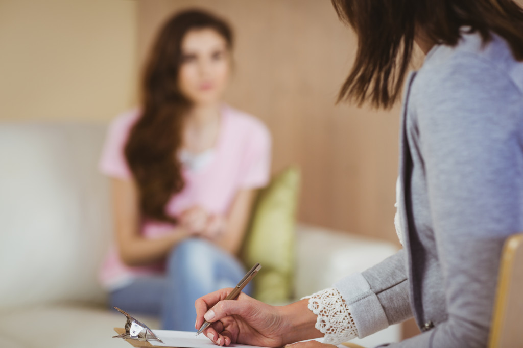 a young female sitting on a sofa talking to a therapist taking notes