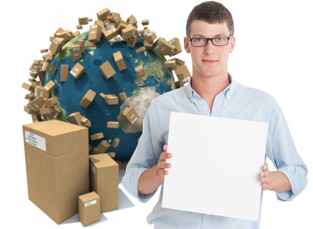 a man holding a blank board and behind him is a picture of the earth with cardboard boxes symbolizing shipping goods