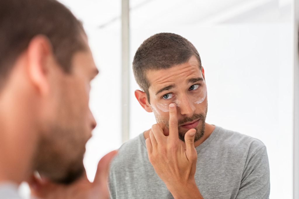 man applying cream in his face for skin care