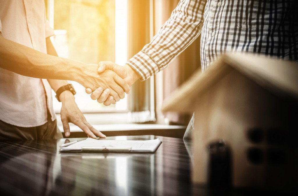 two male people shaking hands in agreement with contract in table and miniature house in the side