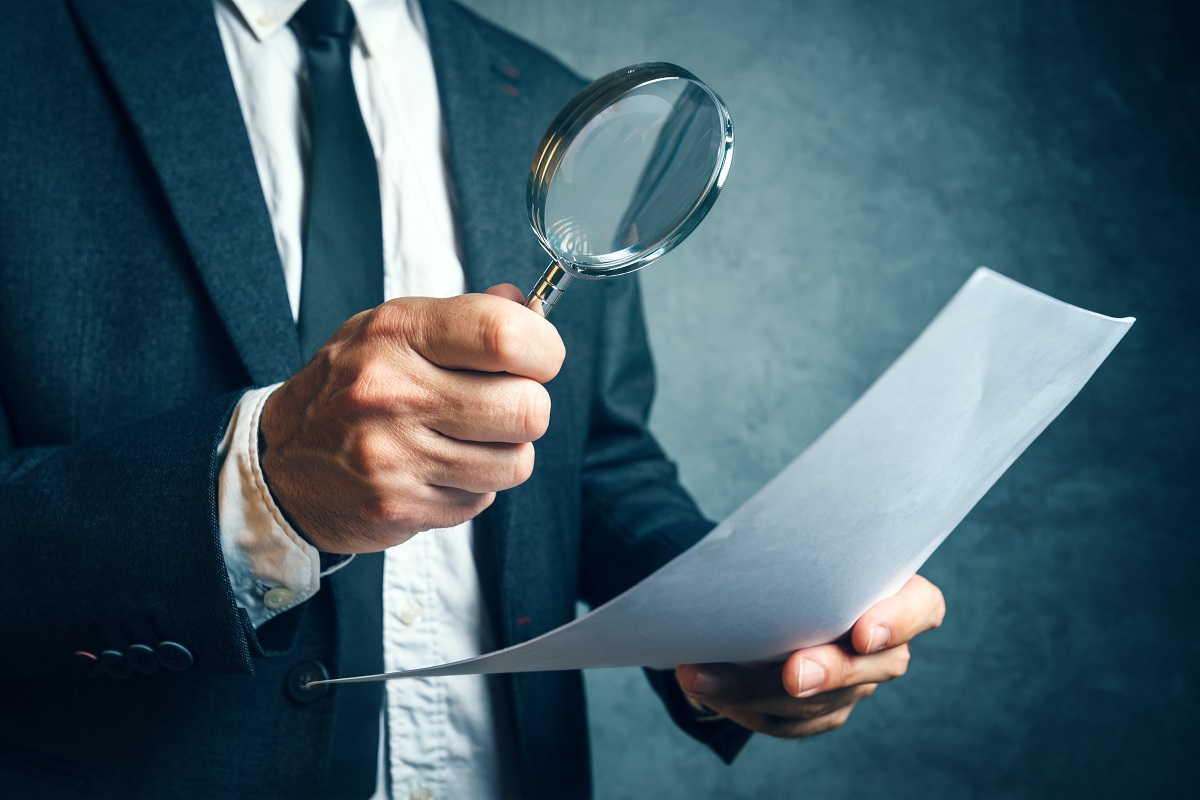 male fiduciary holding a magnifying glass on top of a document to assess it