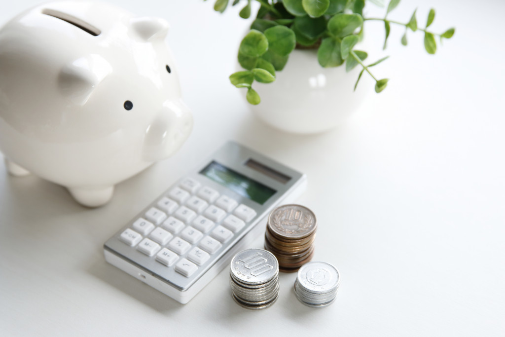 piggy bank, white calculator, and stacks of coins in a white table