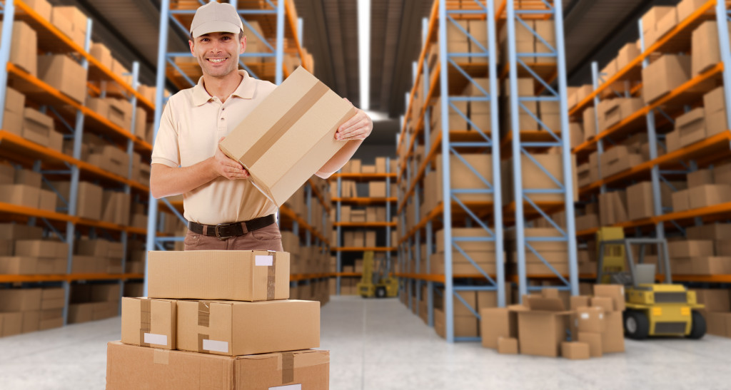 big warehouse for fulfillment center with male worker smiling while carrying a box