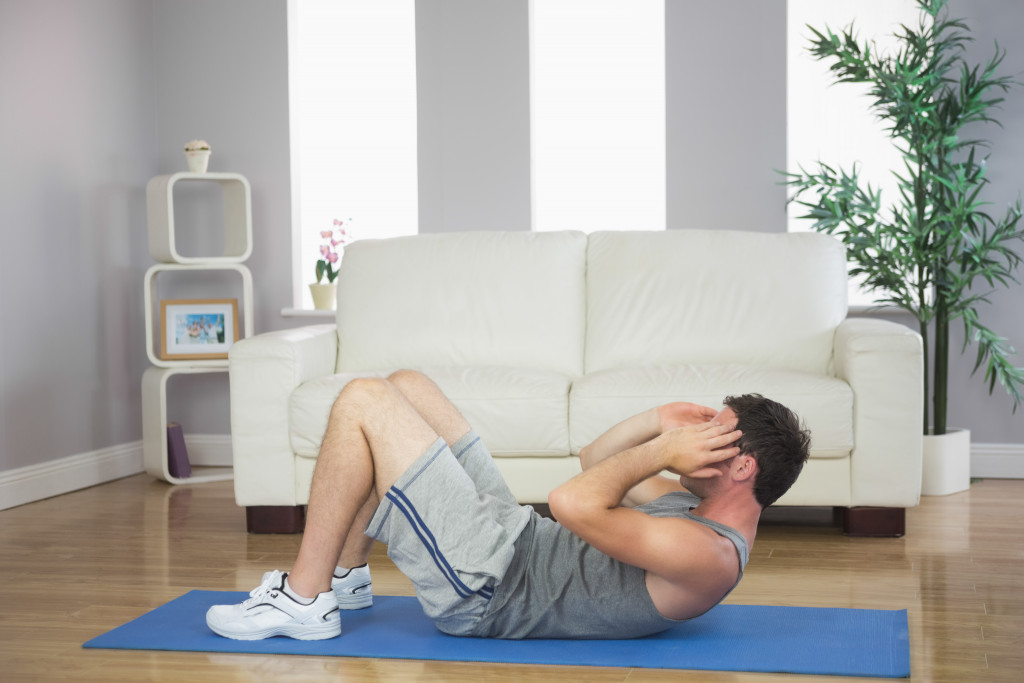 Young man performing crunches in the living room of his home.