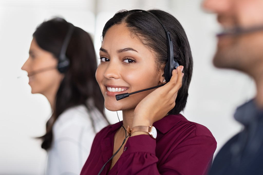 A woman with headphones smiling to the camera while talking to a customer virtually