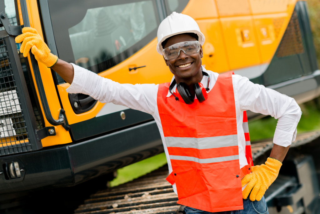 A construction worker smiling beside a construction crane