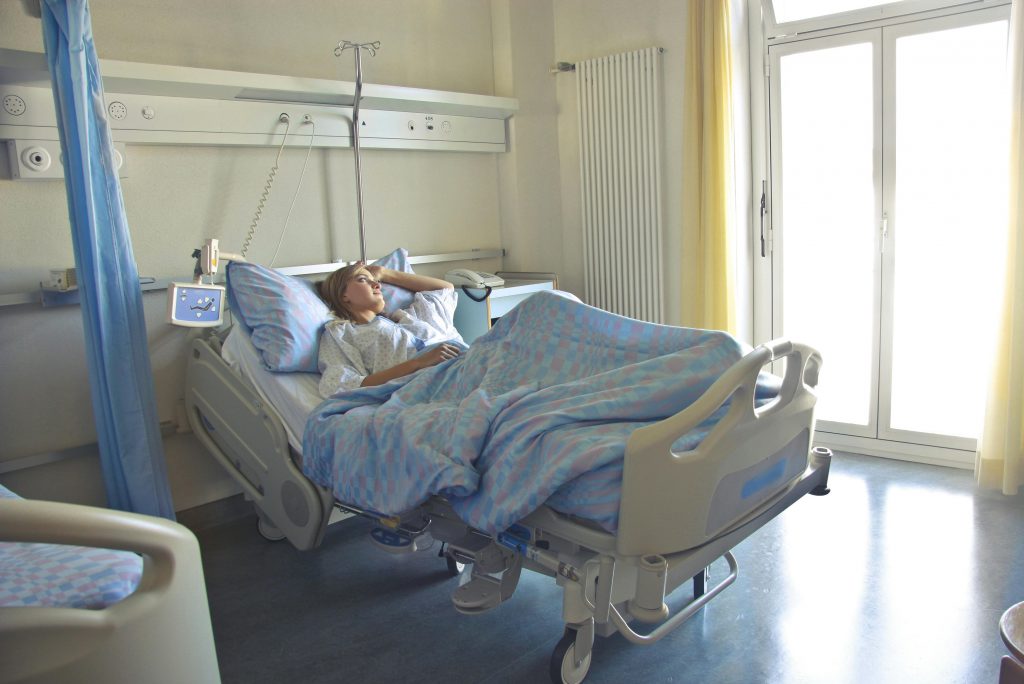 woman looking out a window while lying on a hospital bed